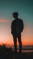 Dramatic silhouette of young Asian male standing against vibrant sunset sky with gradient teal and orange colors, creating moody atmospheric scene at dusk.