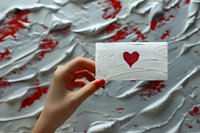 Female hand holding white business card with red heart against textured white wall with red accents, perfect for valentine day marketing, love message or romantic business concept.
