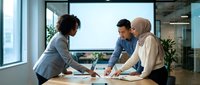 Three diverse business professionals collaborating over documents at modern office table during productive meeting session.
