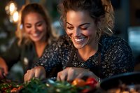 Young Hispanic women in sparkly evening attire preparing food and laughing together in warm ambient lighting, creating joyful atmosphere during holiday dinner party preparation.