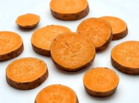 Freshly sliced sweet potato rounds scattered on white background, showing vibrant orange flesh and natural texture for food and nutrition content.