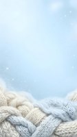 Cozy knitted sweaters and scarves in cream and light blue tones arranged at bottom of frame against soft winter sky with falling snow and sparkles, perfect for seasonal campaigns.