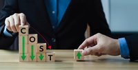 Businessman hands arranging wooden blocks spelling COST with downward arrows showing expense reduction and financial optimization strategy.