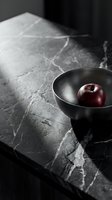 Red apple in metallic bowl on marble surface with dramatic lighting, suitable for food styling and culinary design projects.