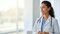 Young Hispanic female doctor in white coat with stethoscope smiling confidently in modern hospital setting with natural lighting for healthcare marketing.