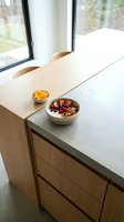 Minimalist kitchen counter with wooden table, concrete countertop, bowl of granola with berries and yogurt, orange slices, natural light from windows, modern dining space.