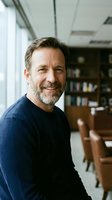 Confident mature Caucasian businessman smiling in modern office library setting wearing navy sweater for corporate leadership and professional success.