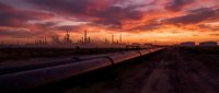 Industrial oil refinery complex with pipeline infrastructure at dramatic sunset with vibrant orange and purple sky colors for energy sector presentations.