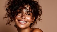 Young woman with curly dark hair and radiant smile against warm brown background, showcasing natural beauty and glowing skin for cosmetic advertising.