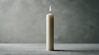 Elegant beige candle burning with warm flame on concrete surface against textured gray wall background for home decor and relaxation atmosphere.
