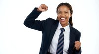 Young African American businesswoman celebrating success with raised fist gesture wearing professional suit and tie on white background.
