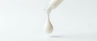Milk pouring from bottle creating droplet against white background, suitable for dairy product packaging and advertising designs.