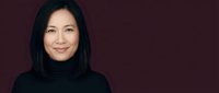Professional Asian businesswoman in black turtleneck smiling confidently against burgundy background for corporate headshots and business presentations.