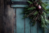 Rustic turquoise wooden door with festive evergreen branch decoration, purple ornament and pine cones creating cozy holiday atmosphere against weathered wood background.