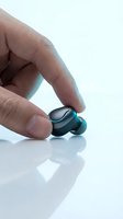 Hand holding black and turquoise wireless earbud against white background, showcasing compact audio technology for music listening and communication.