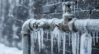 Frozen water pipes with icicles and thermometer showing extreme cold weather conditions causing plumbing problems in winter storm.