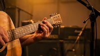 Musician hands playing acoustic guitar in warm studio lighting with microphone stand in background for music recording session.