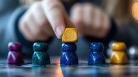 Colorful wooden game pieces arranged in rows on reflective surface with blurred person placing yellow piece on top, creating strategic board game atmosphere.