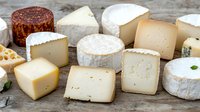 Variety of artisanal cheese wheels and wedges arranged on rustic wooden surface, showing different textures, colors and aging stages of gourmet dairy products.