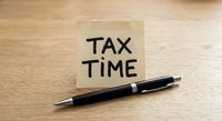 Yellow sticky note with TAX TIME text and black pen on wooden desk surface for financial planning and accounting preparation during tax season.