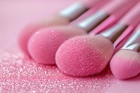 Professional makeup brushes with pink bristles on glittery surface, macro photography showing soft texture and fine details in pastel pink tones.