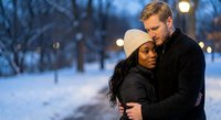 Interracial couple embracing in snowy winter park at twilight with warm lights creating romantic atmosphere for holiday greeting cards and love concepts.