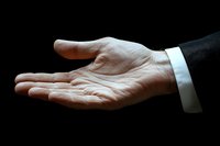 Dramatic side view of an open male hand in business suit with white cuff against black background, palm up in giving or receiving gesture.