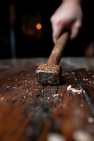 Weathered hammer head with wooden handle resting on rustic wooden surface, dramatic lighting highlights texture and debris from construction work.