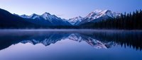 Serene mountain lake with perfect reflections of snow-capped peaks at twilight. Misty waters create mirror effect in peaceful alpine wilderness setting.