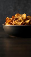Crispy golden persimmon chips in ceramic bowl on dark wooden surface, healthy dried fruit snack for organic food photography and culinary content.
