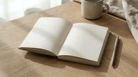 Open blank notebook with pen and coffee mug on wooden desk in natural sunlight creating peaceful workspace atmosphere for writing and planning.