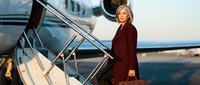 Professional blonde businesswoman in burgundy coat boarding private jet at sunset, luxury travel and corporate aviation concept.