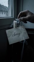 Hand holding a burning sorry note with smoke rising, dark moody atmosphere near rainy window, symbolizing regret, apology, and emotional release.