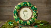 Festive St. Patrick's Day wreath with shamrocks, leprechaun hats and gold coins surrounding Happy St. Patrick's Day message on rustic wooden background.