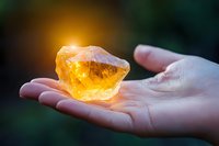 Raw citrine crystal glowing with warm golden light held in open palm against dark background, showcasing natural mineral healing properties.