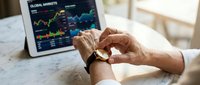 Professional trader analyzing global financial markets on tablet while checking smartwatch for real-time data in modern office workspace.