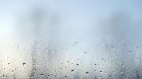 Water droplets on glass window with blurred cloudy sky background creating atmospheric rainy day mood for weather and seasonal concepts.