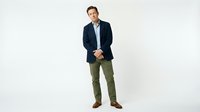 Middle-aged Caucasian male professional wearing navy blazer and olive chinos standing against white background for business and corporate use.