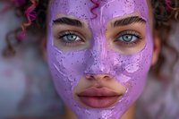 Young woman with bright blue eyes wearing purple glitter face mask during spa treatment. Curly hair and natural makeup visible through cosmetic skincare mask.