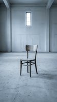 Single wooden chair positioned in empty concrete room with white walls and narrow window, conveying isolation, minimalism, and solitude for conceptual design projects.