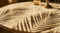 Sunlight casts palm leaf shadows across a marble tabletop with glasses and gold accents, creating elegant tropical ambiance for luxury interior design and hospitality settings.