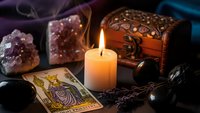Mystical fortune telling setup with tarot cards, burning candle, amethyst crystals, wooden chest and black stones creating atmospheric divination scene.