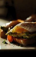 Gourmet sandwich with poached egg, mashed avocado, and black pepper on toasted bread, runny yolk dripping onto fresh vegetables in moody lighting.