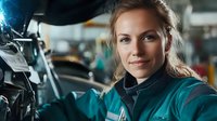 Young Caucasian female auto mechanic with confident smile working in repair garage, wearing teal uniform. Professional woman in traditionally male occupation.