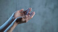 Open cupped hands reaching upward in prayer or receiving gesture against soft gray background for spiritual and wellness concepts.