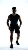 Athletic male with dark skin tone wearing black sleeveless shirt and shorts, hands on hips in confident stance against white background. Suitable for fitness, wellness, and sportswear marketing.