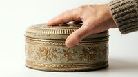 Caucasian male hand opening ornate vintage brass box with floral relief detailing, antique storage container for jewelry, keepsakes, or decorative home accessories.