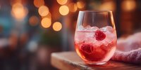 Refreshing raspberry cocktail with ice in stemless glass on wooden surface with warm bokeh lights background for bar and restaurant menus.