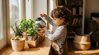 Young child with curly hair watering potted herbs on wooden windowsill in bright kitchen, learning gardening skills and plant care at home.