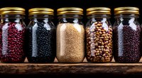 Glass jars filled with various dried legumes and grains on wooden shelf, including red kidney beans, black beans, quinoa, chickpeas and lentils, with gold lids.